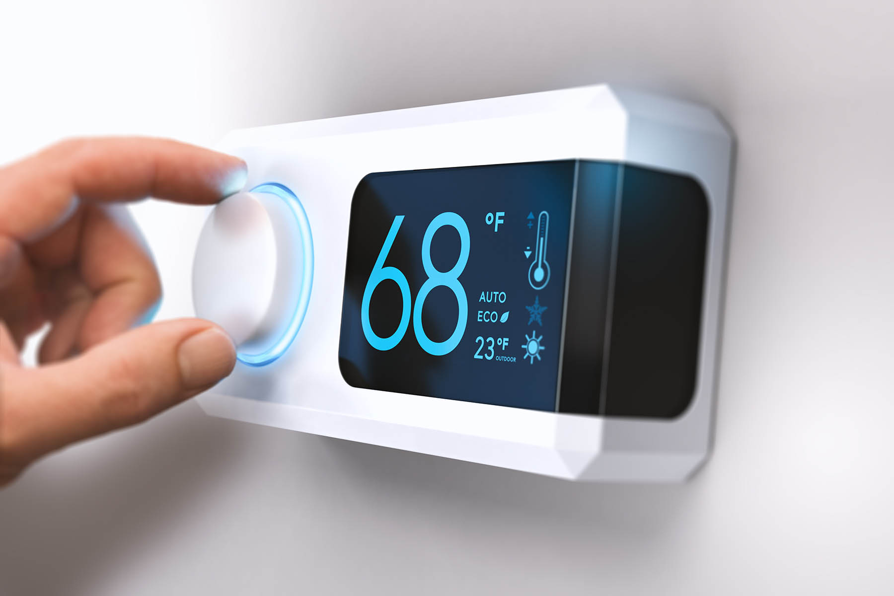 Hand turning a home thermostat knob to set temperature on energy saving mode.