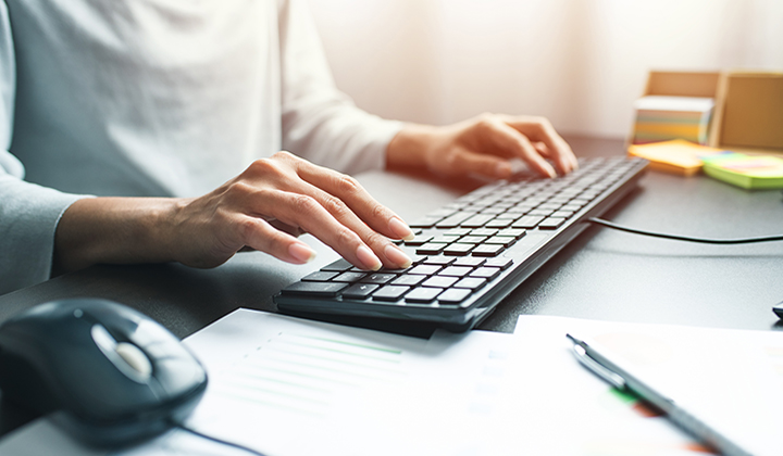 Business woman hand with computer mouse and keyboard with document graph paper and pen on table at office day time.