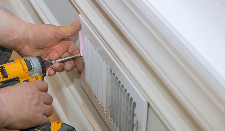 Man is holding hand drill in hands installing wall vents.