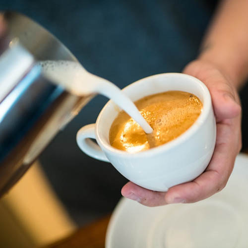 Pouring milk into coffee cup making a latte.