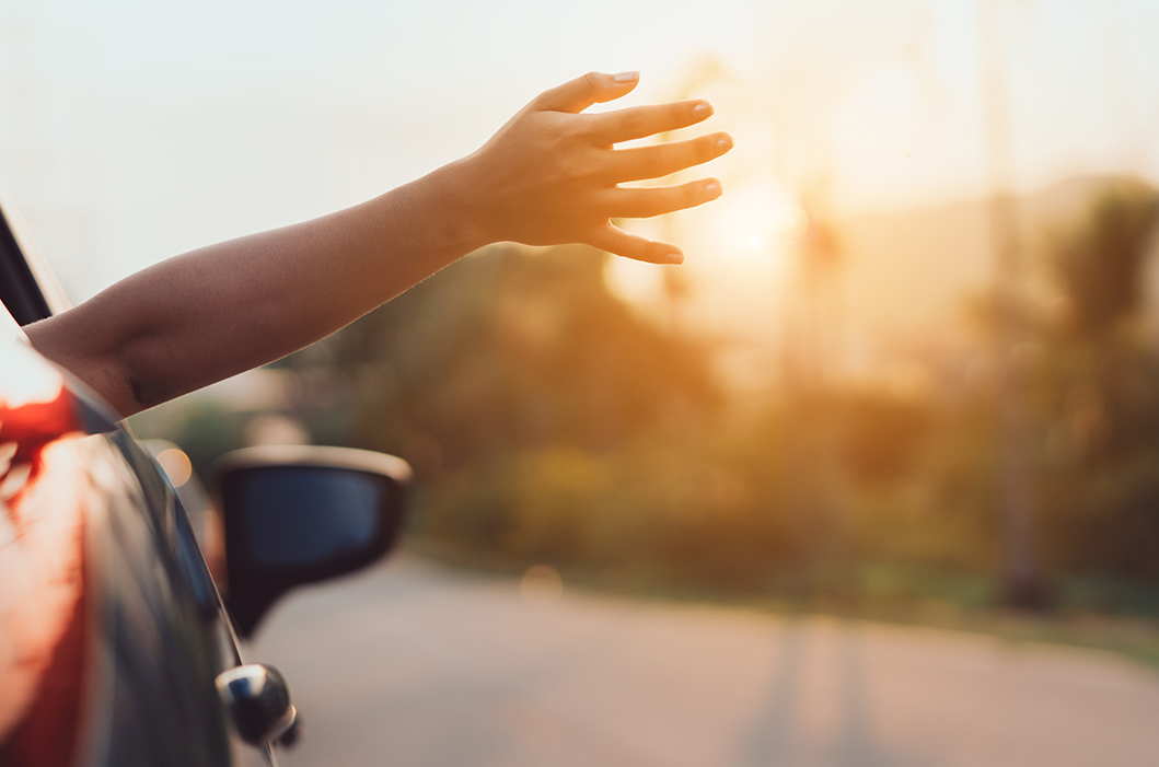 Electric vehicle driving into the sunset, feeling of happiness with hand waving out the window in the wind.