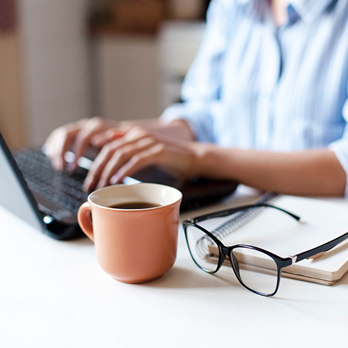 Close up of woman hands working on her laptop in the kitchen with a cup of coffee by her side.s.