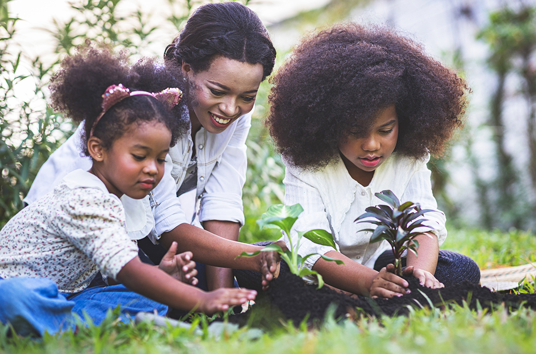 Mother and two daughters planting trees/plants in their yard on a spring day.