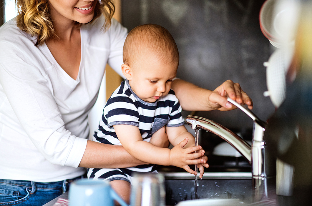 Young mother with baby boy washing up the dishes with warm water from heat pump water heater.